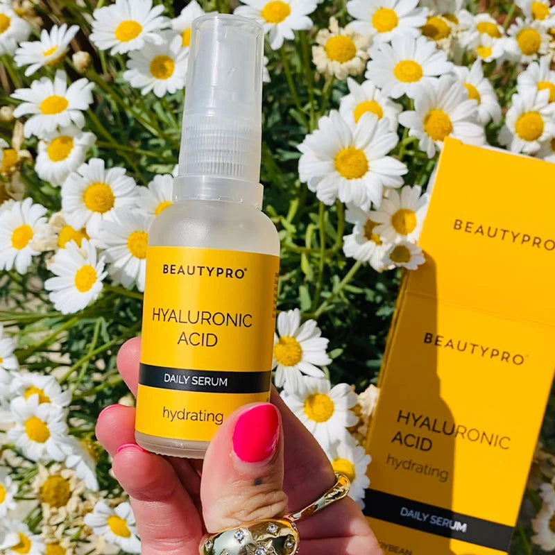 Beautypro hyaluronic acid Serum bottle held in hand with chamomile flowers in background