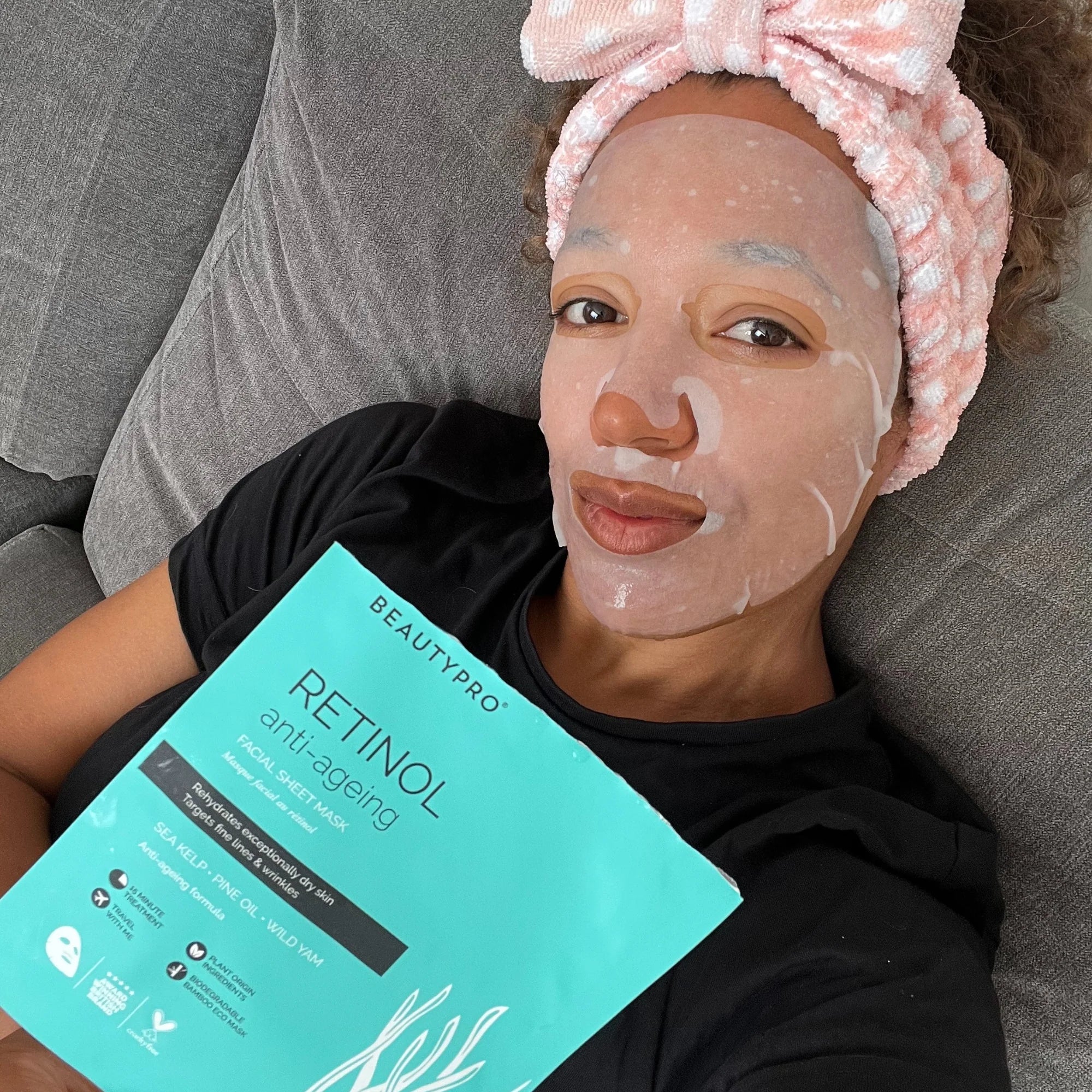 User lounging with sheet mask on and holding product