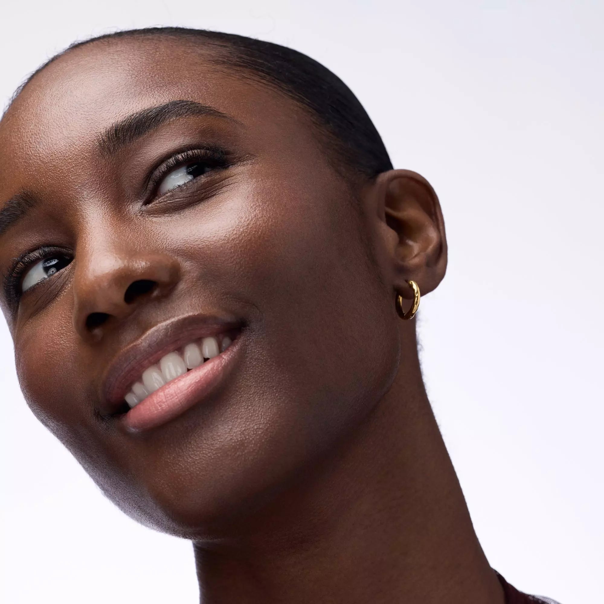 Model with deep skin tone wearing Catrice Blushin’ Charm Multi Stick Sparkle Lover for radiant glow