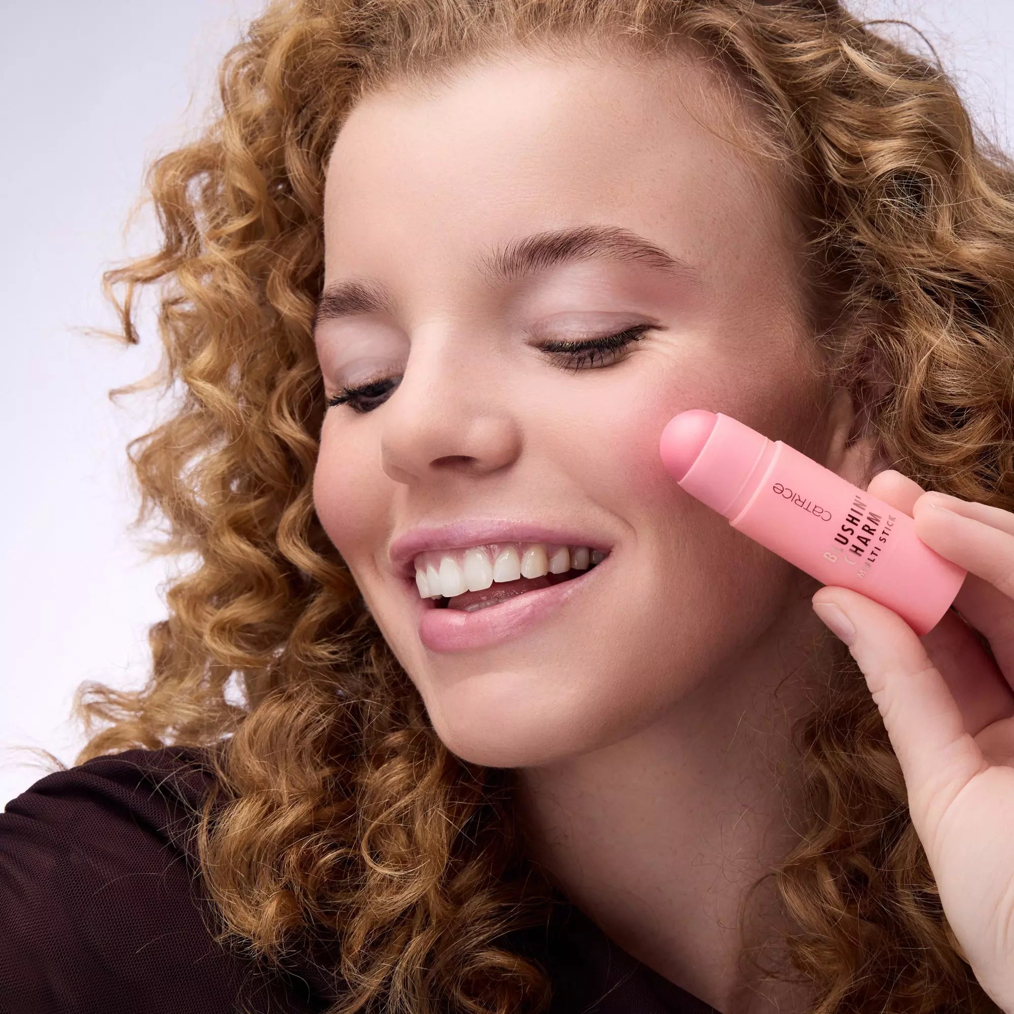 Model with light skin applying Catrice Blushin’ Charm Sparkle Lover blush stick on cheeks
