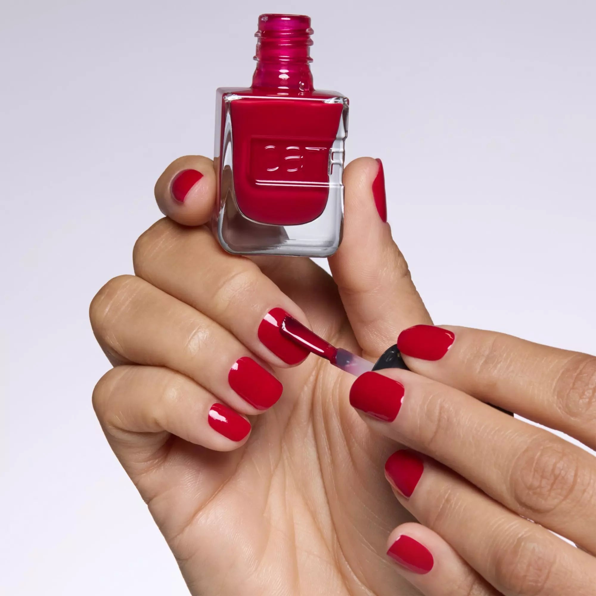Manicured hand holding Catrice red gel-effect nail polish bottle in Rasberry Pie 