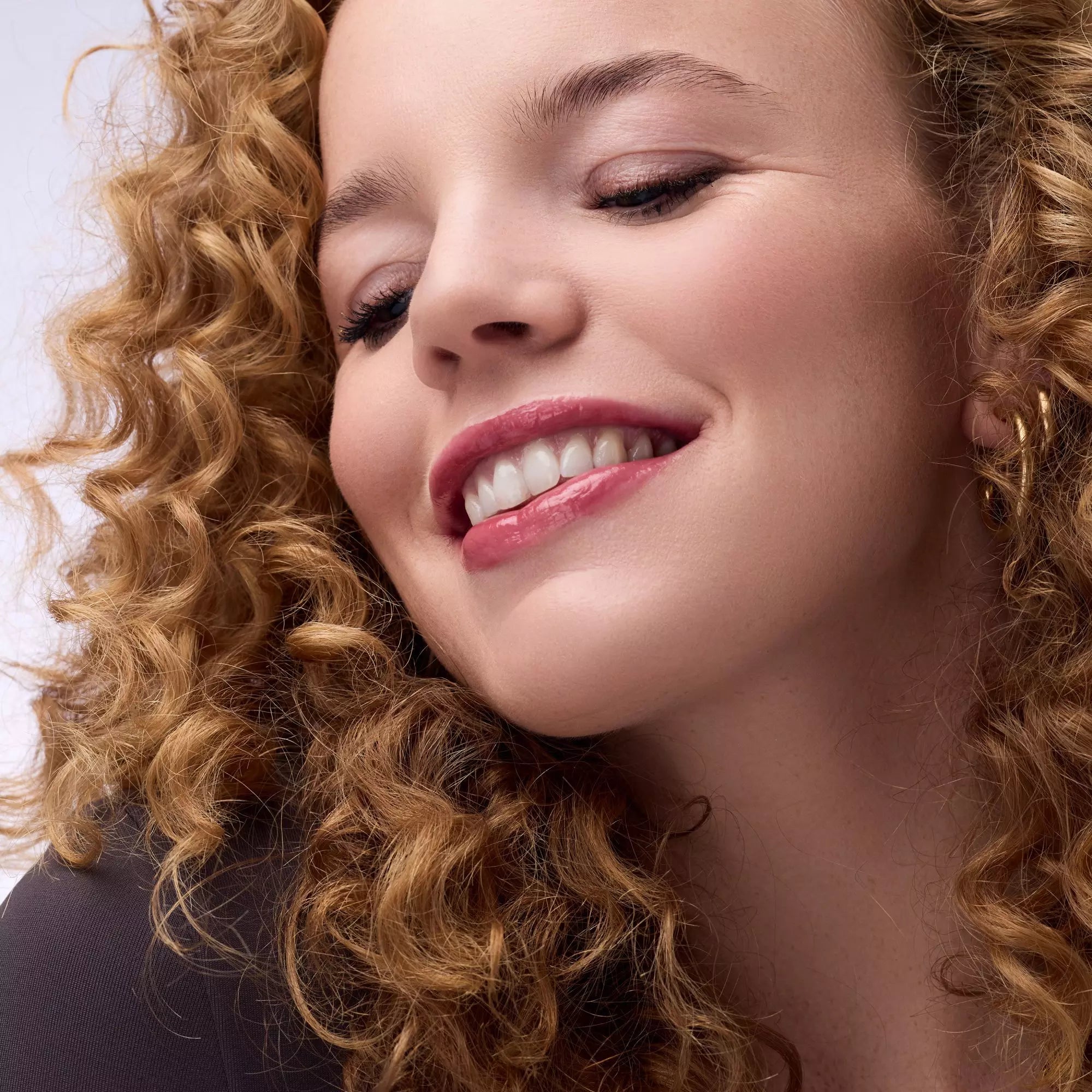 Fair-skinned model smiling with Catrice 040 plumping mauve lip gloss