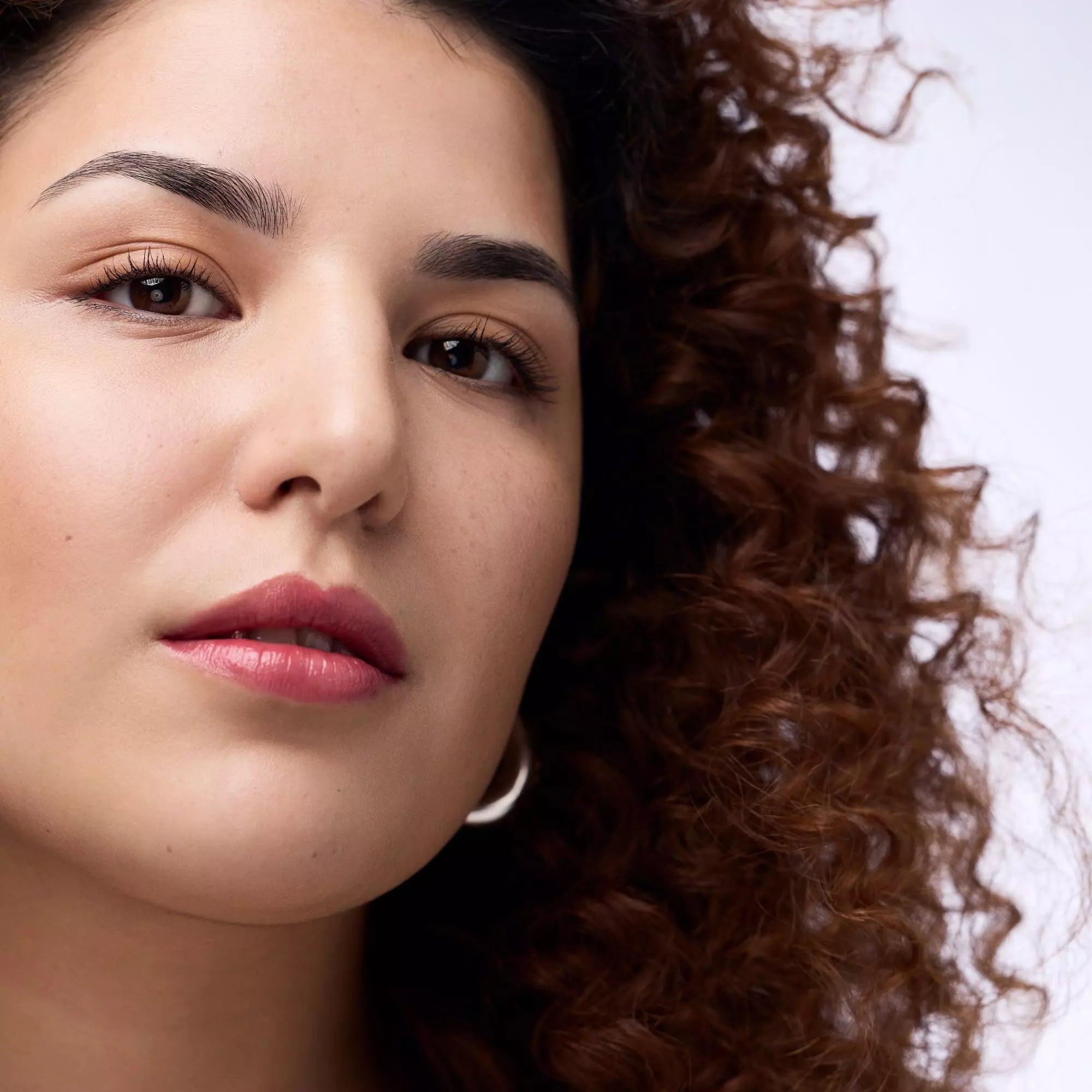 Model with defined curls wearing glossy Catrice Melt & Plump lip colour 040