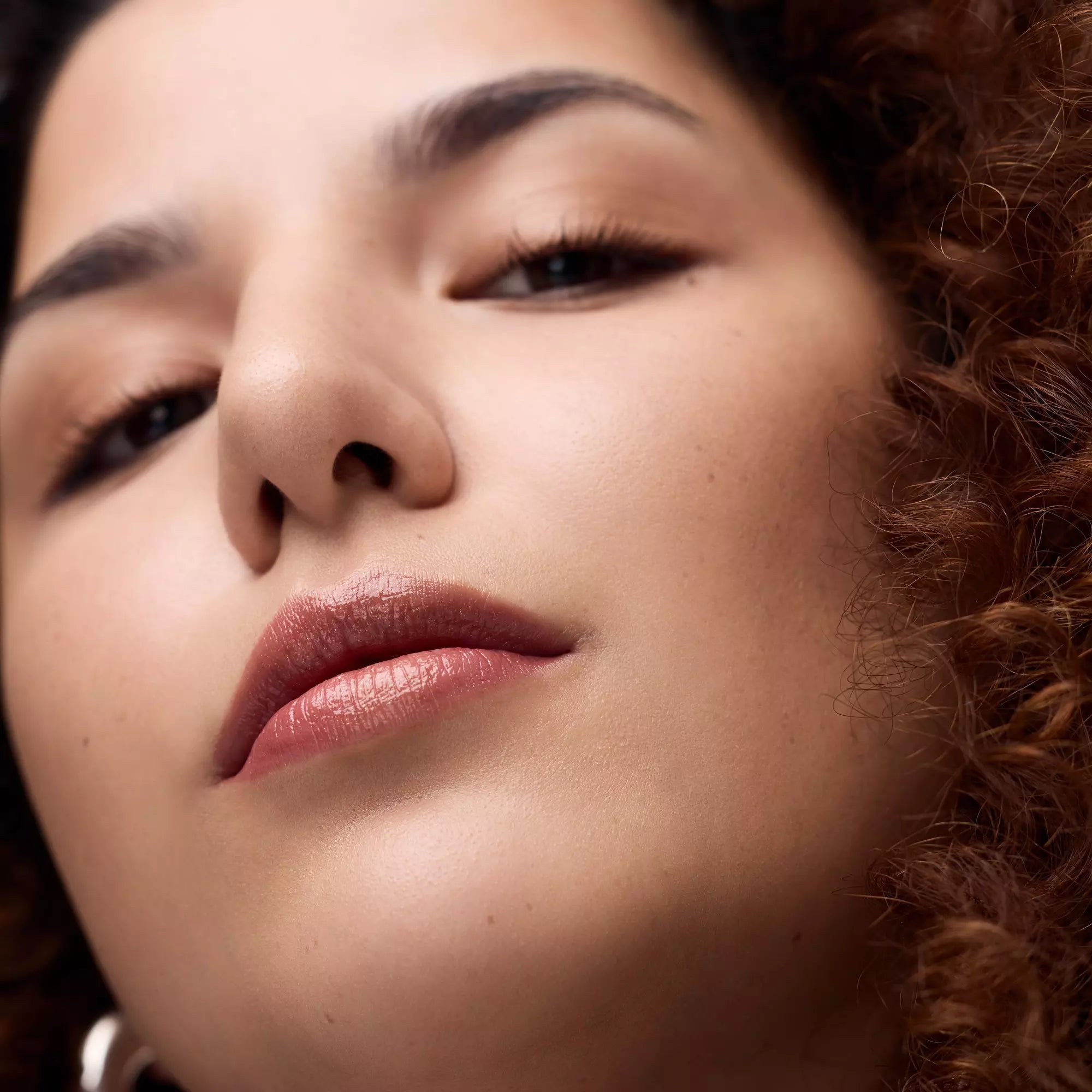 Smiling model with curly hair wearing Catrice Melt & Plump 030