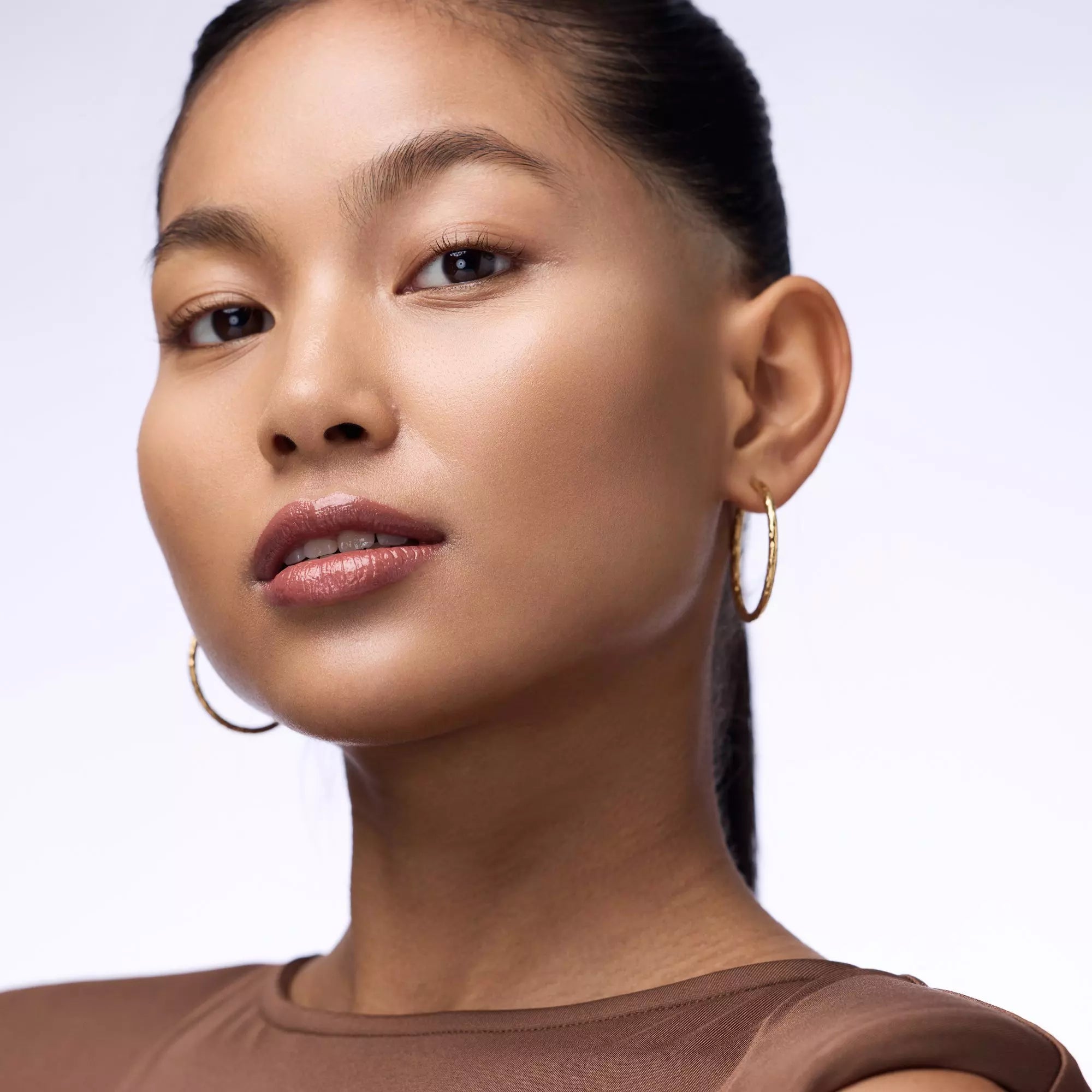 Model with hoop earrings wearing Catrice 030 Tipsy In Love lip gloss