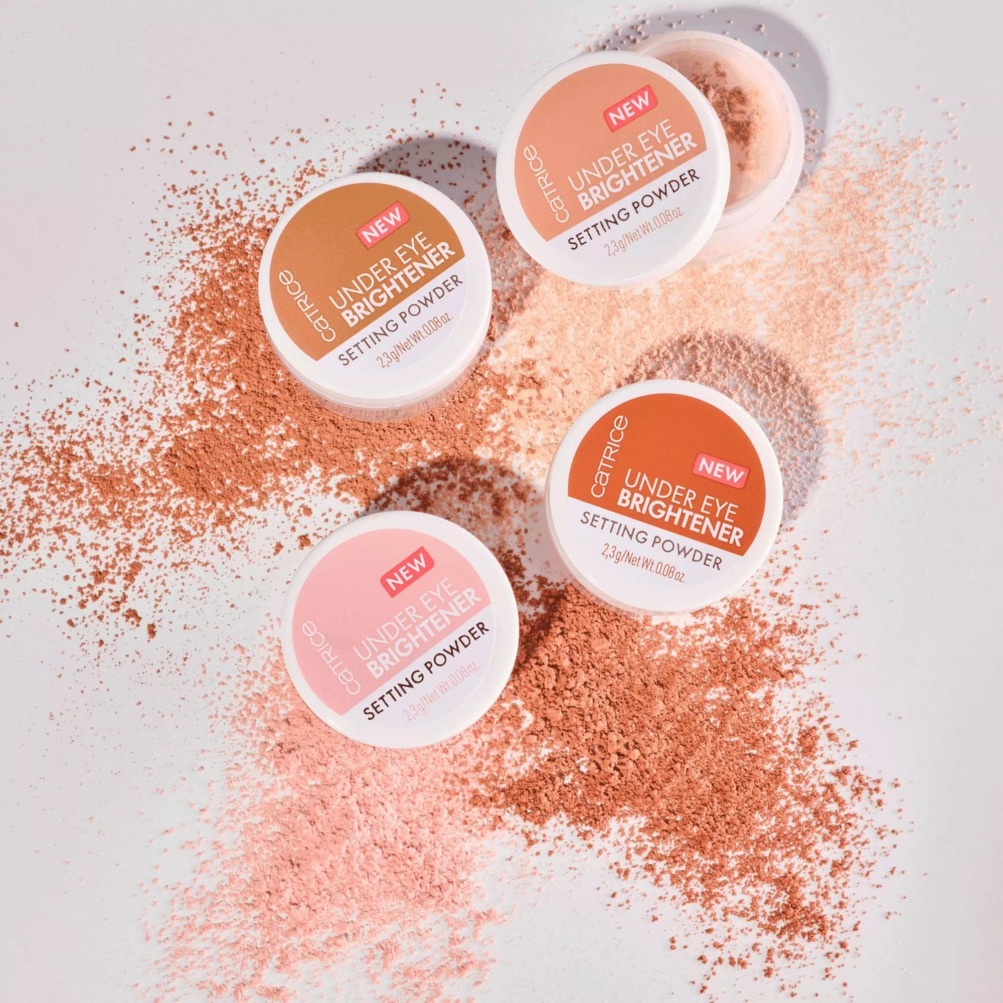 Group of Catrice Under Eye Brightener Setting Powder Colours on pink background with powder scattered