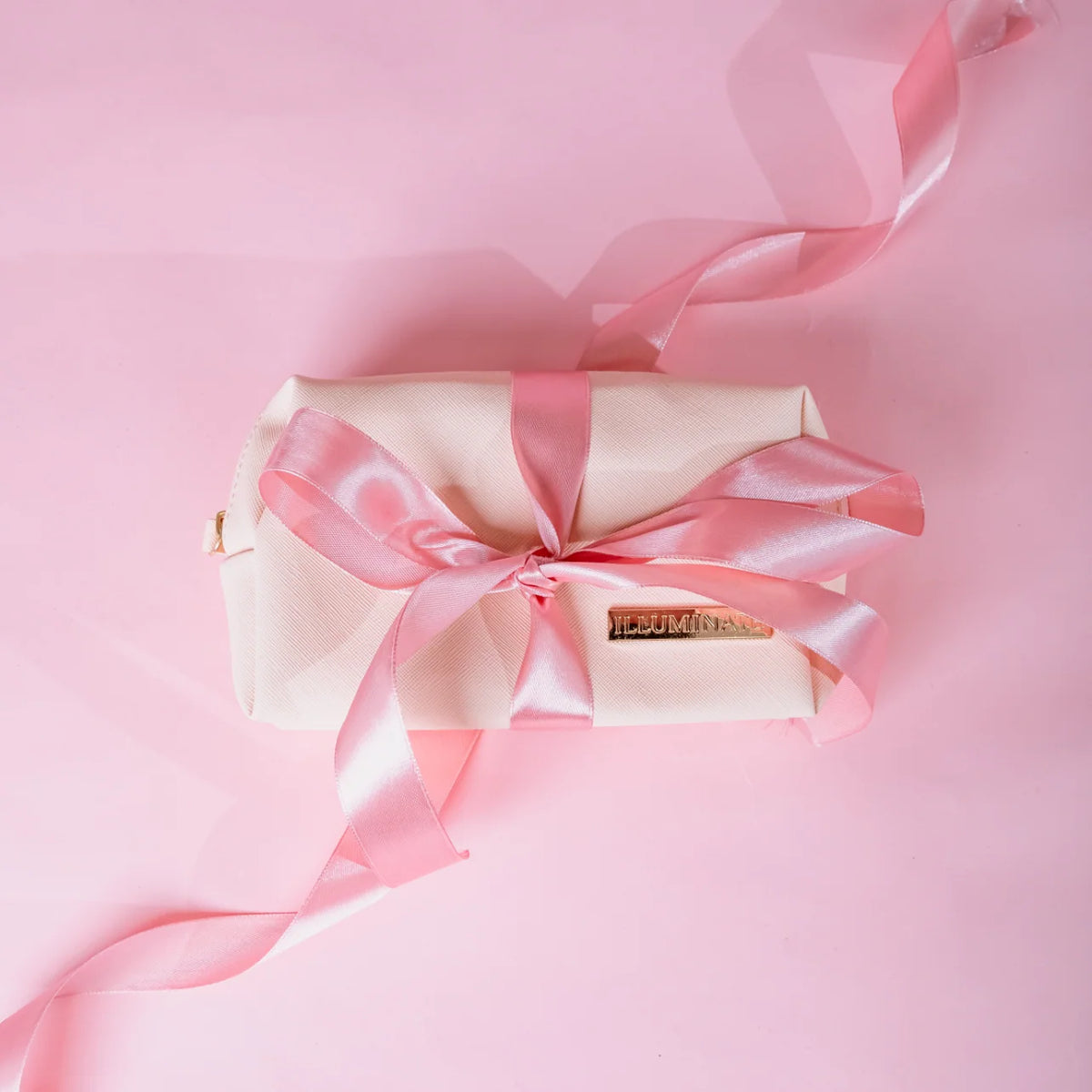 Illuminate by Shauna pink beauty makeup bag wrapped with satin ribbon against a pink background