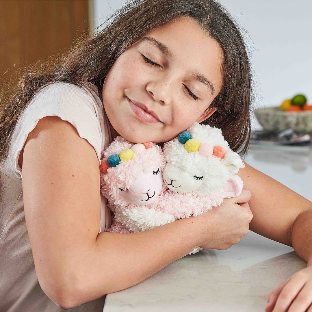 Child hugging Warmies llamas — reheatable lavender plush used for calming, bedtime and sensory comfort.